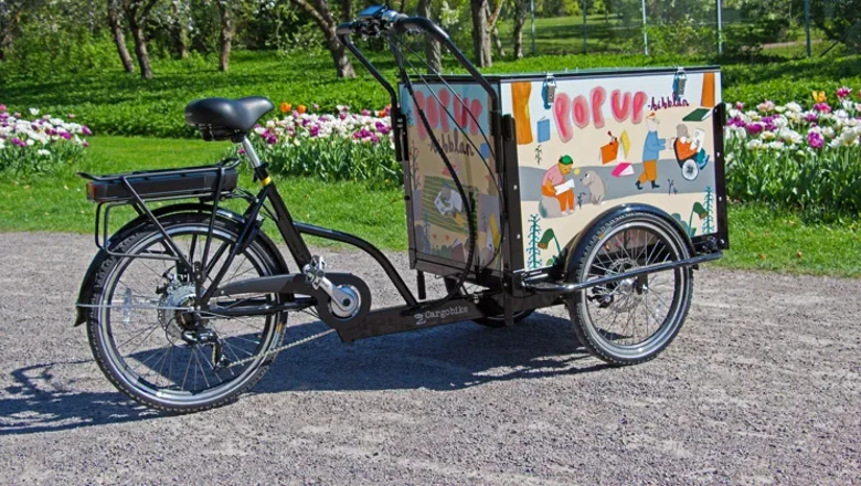 Bibliotekets lådcykel parkerad framför en blomrabatt utanför Huvudbiblioteket.