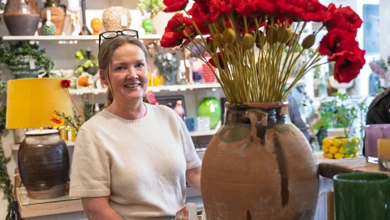 Helén står bredvid en stor vas med röda blommor i sin butik