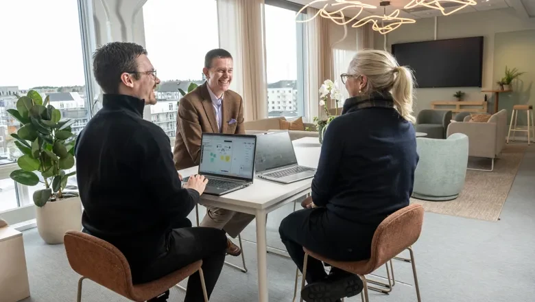 Erric sitter runt ett bord med två kollegor med bärbara datorer.