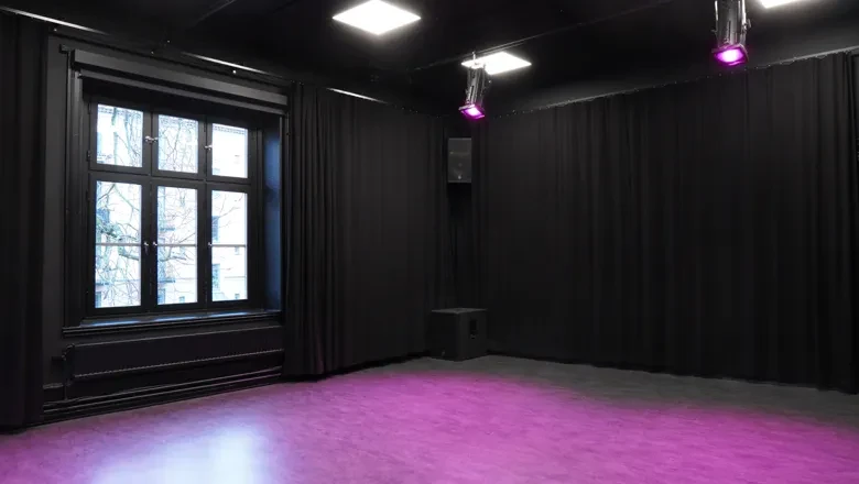 Ett tomt rosafärgat golv i ett rum med ett stort äldre fönster och vita lampor i taket