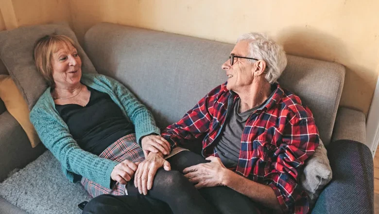 An older couple smiling and talking at home in their couch
