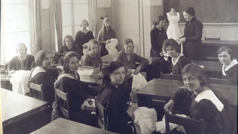 En grupp flickor som sitter vid bänkar i ett klassrum och har lektion i syslöjd.