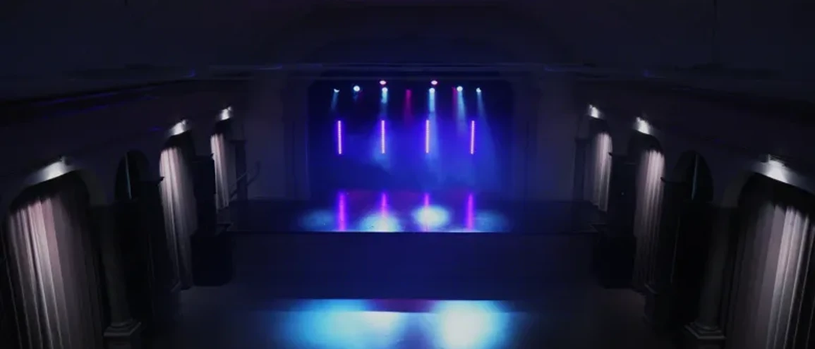 Tom konsertlokal med draperier vid sidorna och blå  och rosa belysning.