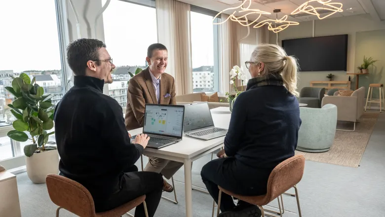 Erric sitter runt ett bord med två kollegor med bärbara datorer.