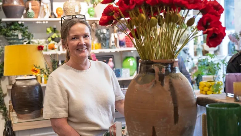 Helén står bredvid en stor vas med röda blommor i sin butik